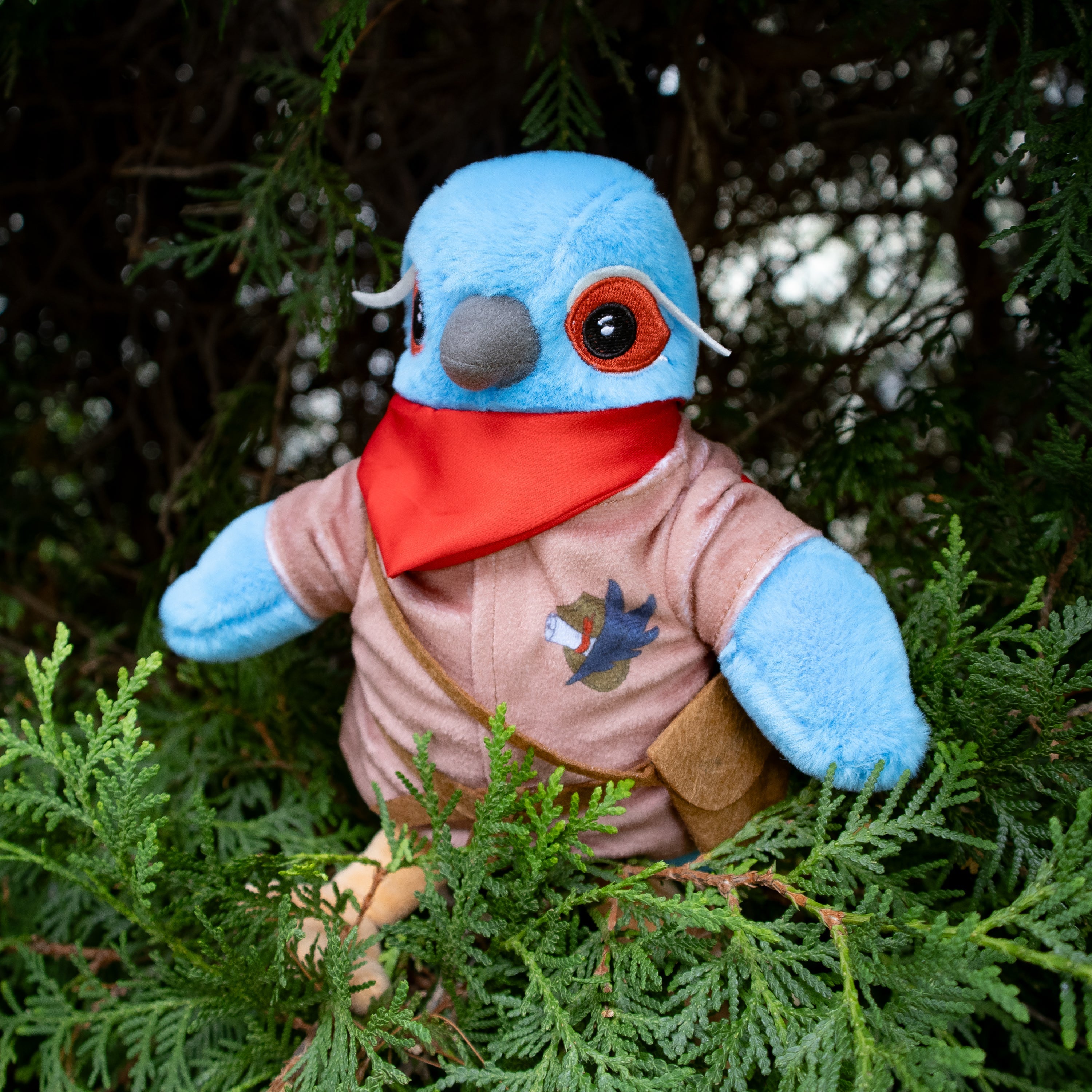 Plush toy with a blue head and red bandana sitting among green foliage